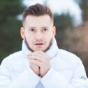 Chilling young man keeping his hands by mouth and warming them up on wintery day