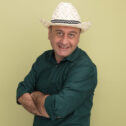 pleased middle-aged man wearing green t-shirt and hat crossing hands isolated on olive green background